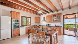 A kitchen with wooden cabinets, a dining table, and chairs, with a view to the outside. - Villa 'Can Rito Nou' with Mountain View, Wi-Fi and Air Conditioning (Felanitx)