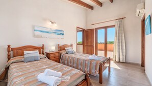 A bedroom with two wooden beds, a painting of a beach, and a view of the outdoors. - Villa 'Can Rito Nou' with Mountain View, Wi-Fi and Air Conditioning (Felanitx)