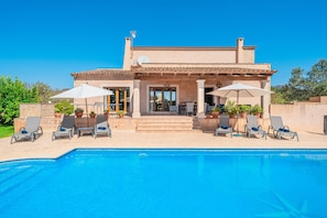 A house with a swimming pool, lounge chairs, and umbrellas.