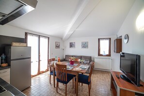 A compact kitchen with a refrigerator, dining table, chairs, and a television. - Bed and Breakfast 'Dolce Alba' with Private Garden, Wi-Fi and Air Conditioning (Montecastrilli)