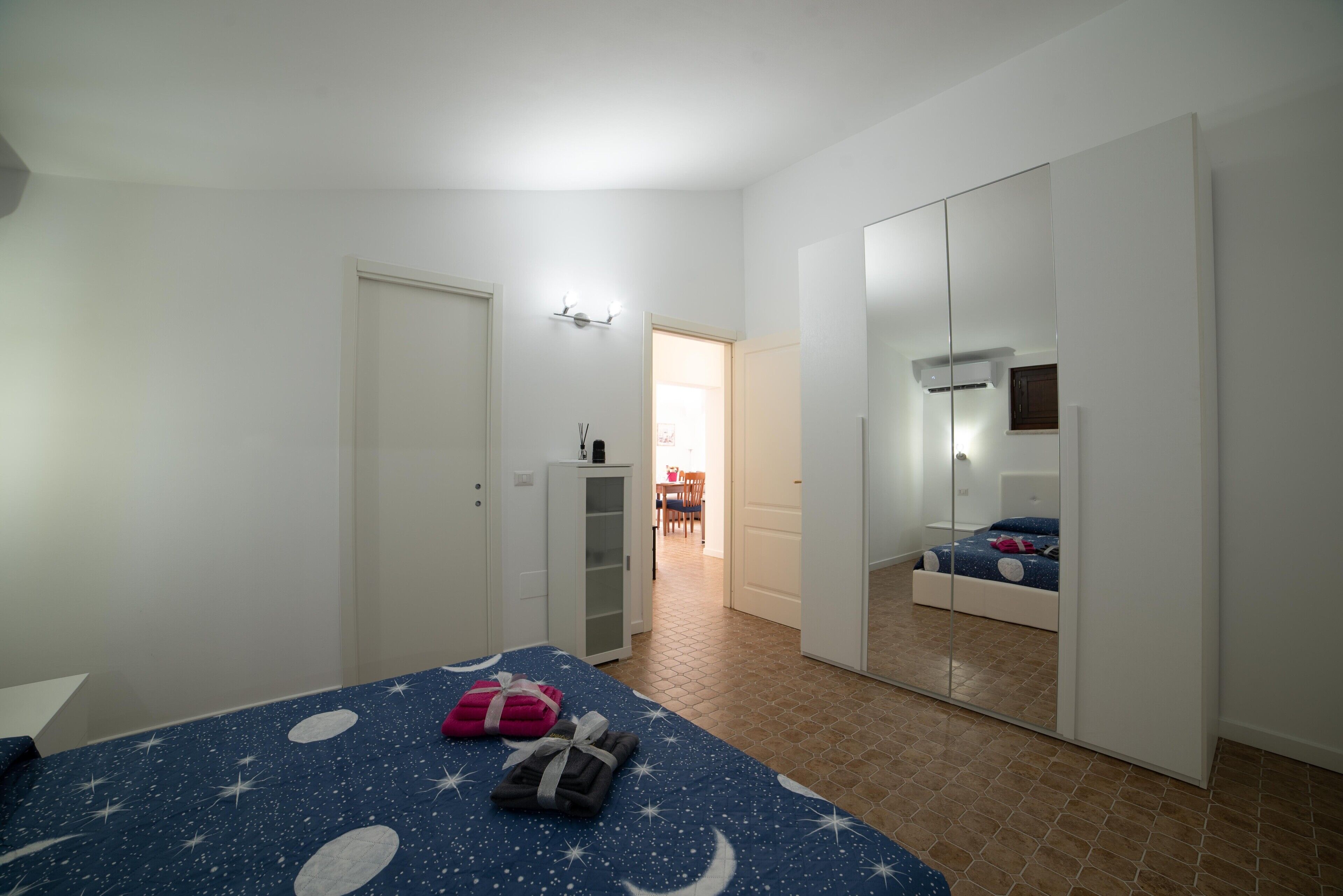 Ein Schlafzimmer mit Bett, Kleiderschrank, Spiegel und einer Tür zum Essbereich.