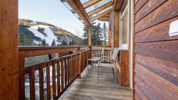 A wooden deck with a glass railing, a table, and a chair. - Apartment 'Antersi Robbi' with Mountain View, Shared Garden and Wi-Fi (St. Vigil Enneberg)