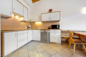 Una cocina con gabinetes blancos, lavavajillas, microondas y comedor con mesa y sillas.