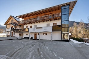 Un immeuble à plusieurs étages doté d’un balcon en bois, de grandes fenêtres et, au loin, d’une piste de ski.