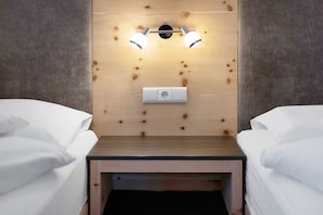 A bedroom with two beds, a wooden headboard, a nightstand with a lamp, and a power outlet.