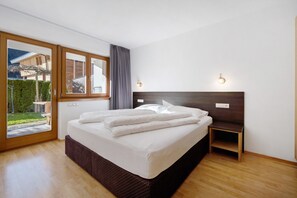 A bedroom with a large bed, a nightstand, a window with curtains, and a view of the outside.