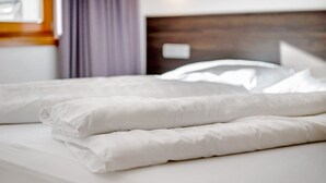 Ein ordentlich bezogenes Bett mit weißen Leinen und Kissen, ein hölzerner Kopfteil und ein Fenster mit Vorhängen.