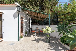 A covered outdoor seating area with a table and chairs, surrounded by potted plants and a white building. - Pool, BBQ, 7 min drive to the beach on an avocado & mango estate, 15 min from Málaga center (Málaga)