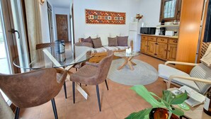A modern living room with a glass coffee table, brown leather chairs, a sofa with patterned cushions, a kitchen area with wooden cabinets, and a decorative wall hanging. - Pool, BBQ, 7 min drive to the beach on an avocado & mango estate, 15 min from Málaga center (Málaga)