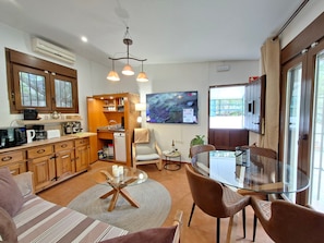 A compact living space with a kitchenette, a dining area with a glass table, and a TV mounted on the wall.