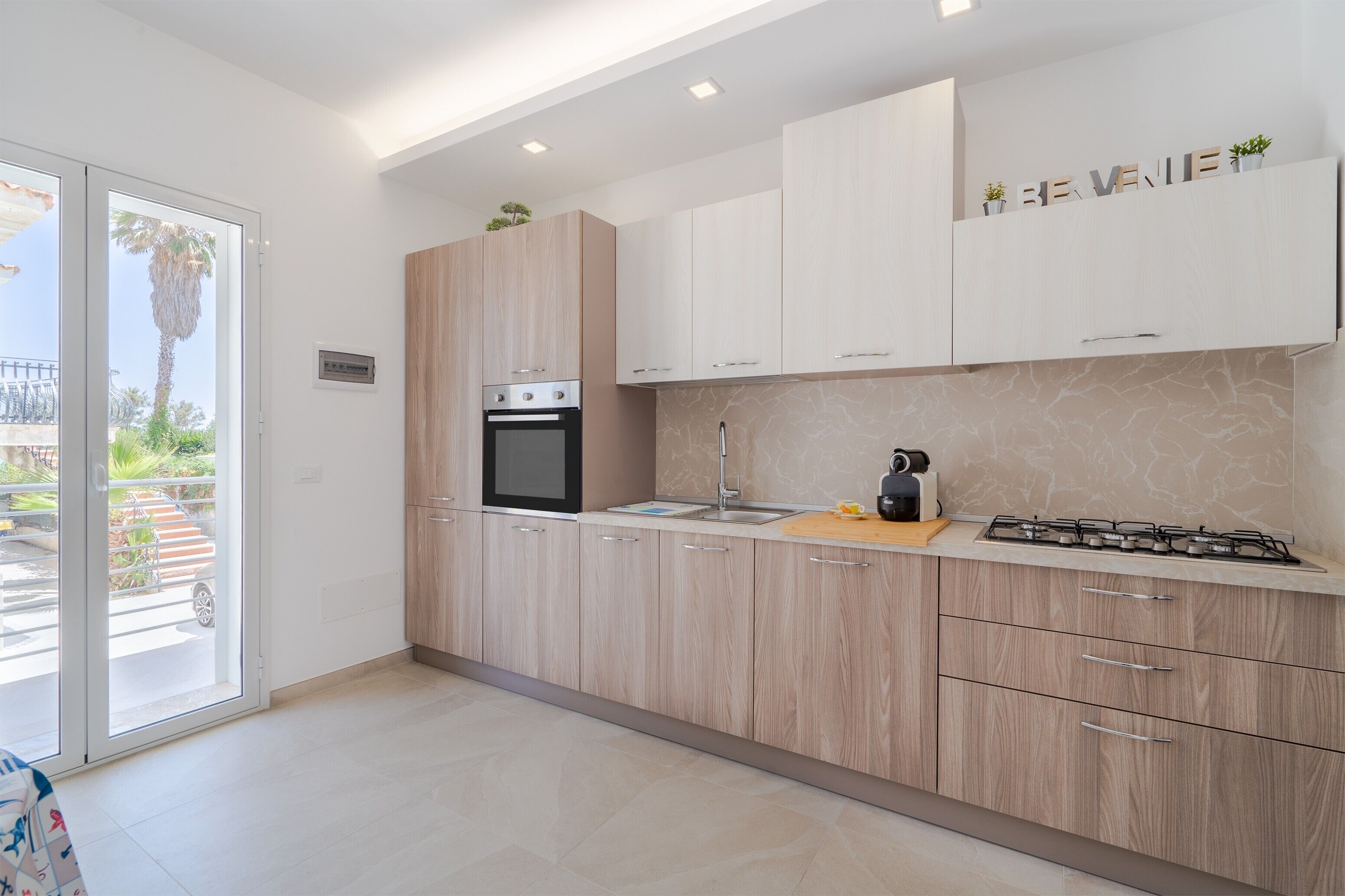 Una cocina moderna con armarios de madera clara, horno empotrado, cocina a gas y un lavaplatos.