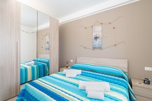 A bedroom with a large mirror, a bed with striped bedding, a nightstand with a lamp, and a wall decoration.