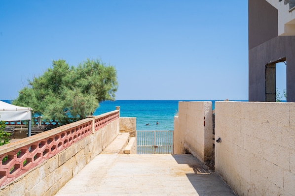 Une vue sur la côte, avec un ciel dégagé, un sentier menant à la mer et un bâtiment dont on aperçoit une fenêtre.