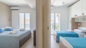 A modern hotel room with two beds, a balcony, and a view of the city. - Holiday Apartment "Greta Vista Mare" with Sea View, Private Terrace & Wi-Fi (Lido di Noto)