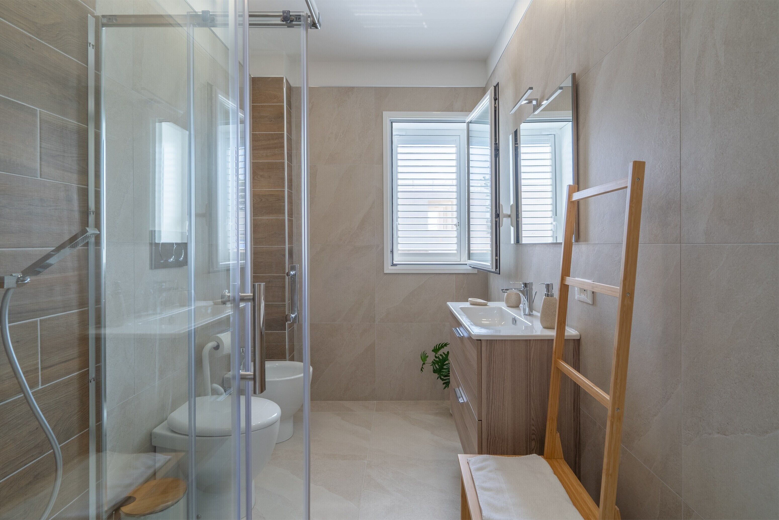 Een moderne badkamer met een glazen douchecabine, een toilet, een wastafel en een houten opbergmeubel.