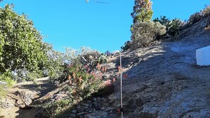 Un patio de piedra con dos sillones blancos, una ladera rocosa y vegetación escasa.