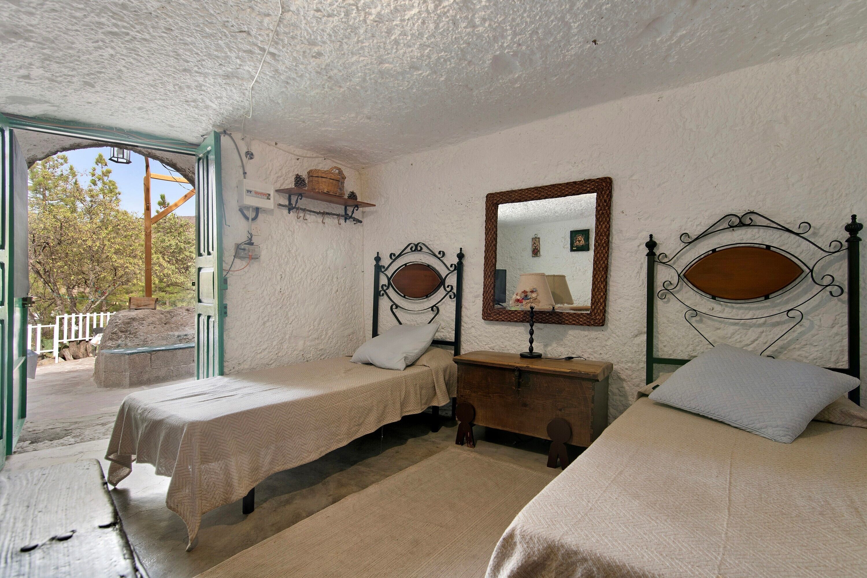 Una habitación con dos camas, un aparador de madera, un espejo y una ventana con vistas a árboles.