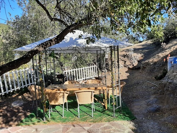 A covered outdoor seating area with a table and chairs, surrounded by a white fence, under a tree. - Vacation Home 'La Cuevita De Hilario' with Mountain View, Private Terrace and Private Garden (Artenara)