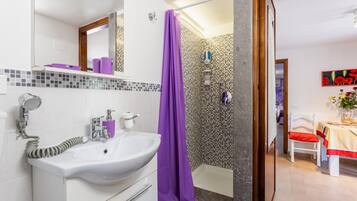 Een badkamer met een witte wastafel, een paars douchegordijn en een betegelde douche.