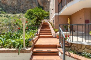 A staircase leading to a building with a stone wall, a statue, and potted plants.