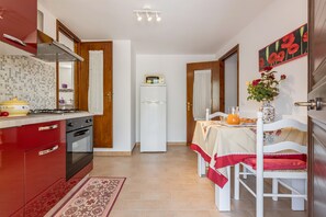 Una cocina compacta con estufa, horno y refrigerador, un área de comedor con mesa y sillas, y un jarrón decorativo con flores.