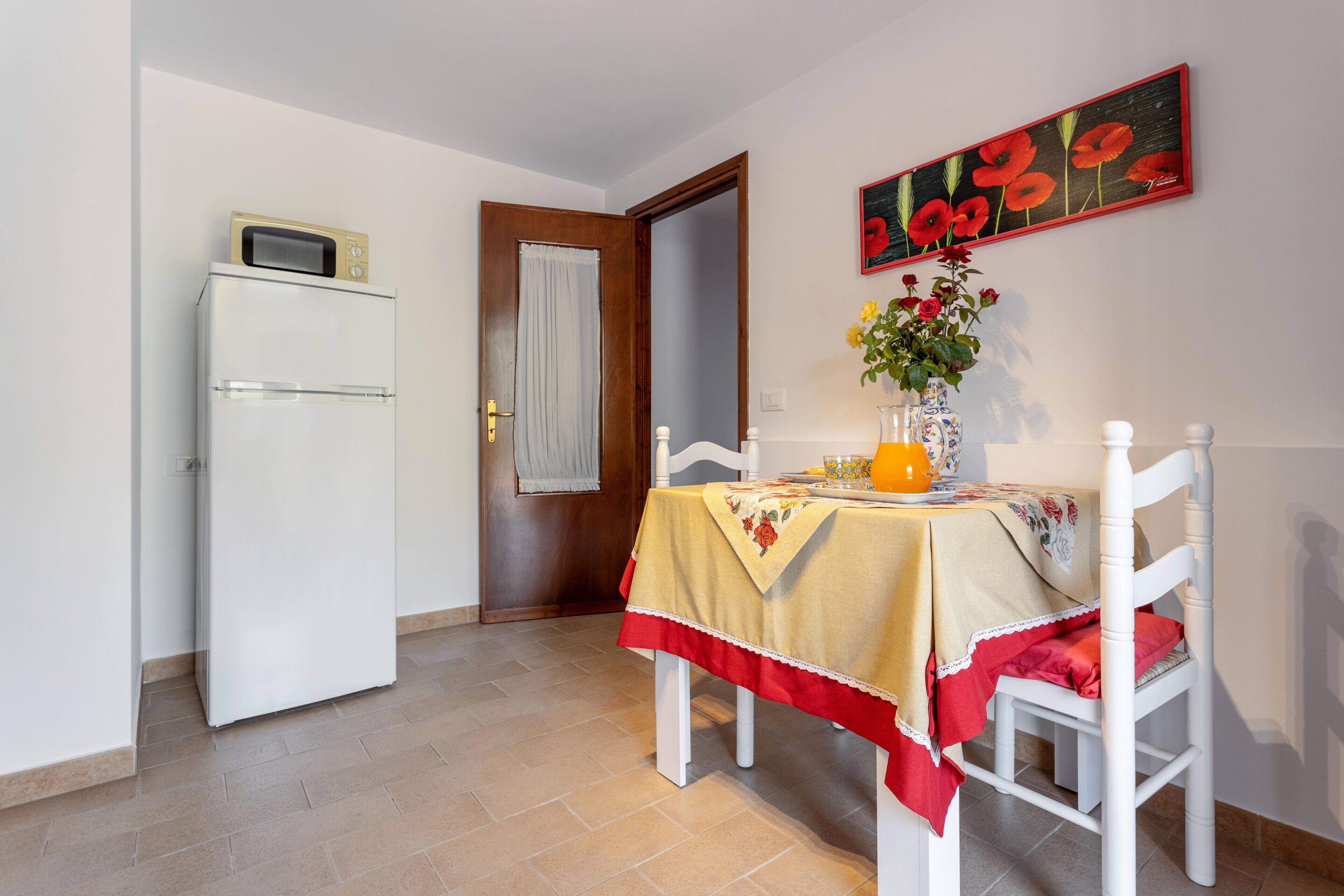 Un coin repas avec une table dressée pour deux personnes, un réfrigérateur blanc et une porte donnant sur une autre pièce.