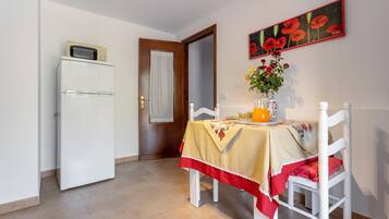 Un coin repas avec une table dressée pour deux personnes, un réfrigérateur blanc et une porte donnant sur une autre pièce.