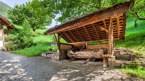 Une construction rustique en bois, dotée d’un toit en pente, entourée de verdure et d’un mur de pierres.