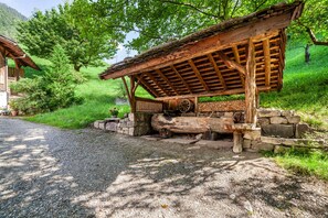 Une construction rustique en bois, dotée d’un toit en pente, entourée de verdure et d’un mur de pierres.