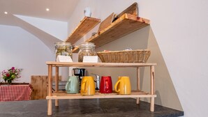 A wooden shelf with jars, a basket, and colorful mugs on a countertop.