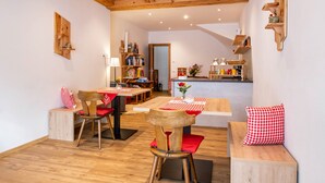 A cozy dining area with wooden furniture, a bookshelf, and a kitchen in the background.