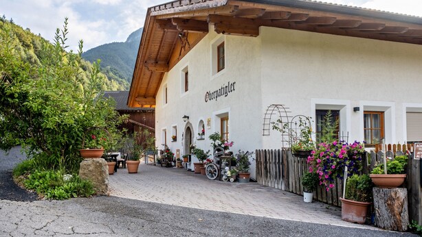 A traditional building with a sign reading 'Oberpatizinger,' surrounded by potted plants and a wooden fence.
