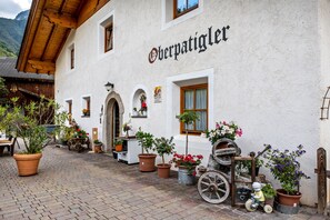A traditional building with a sign reading 'Oberpatigler.' It features a cobblestone courtyard with potted plants and a vintage cart.