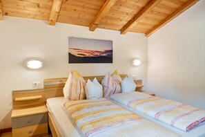 Une chambre avec un plafond en bois, un lit avec une literie à rayures, une table de chevet et une commode, ainsi qu’un tableau accroché au mur.
