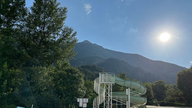 Une piscine avec un toboggan aquatique, une plateforme de plongeon et une montagne en arrière-plan.