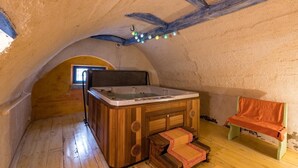 Un bain à remous dans une chambre mansardée au décor rustique, avec des poutres en bois, un banc et une fenêtre.