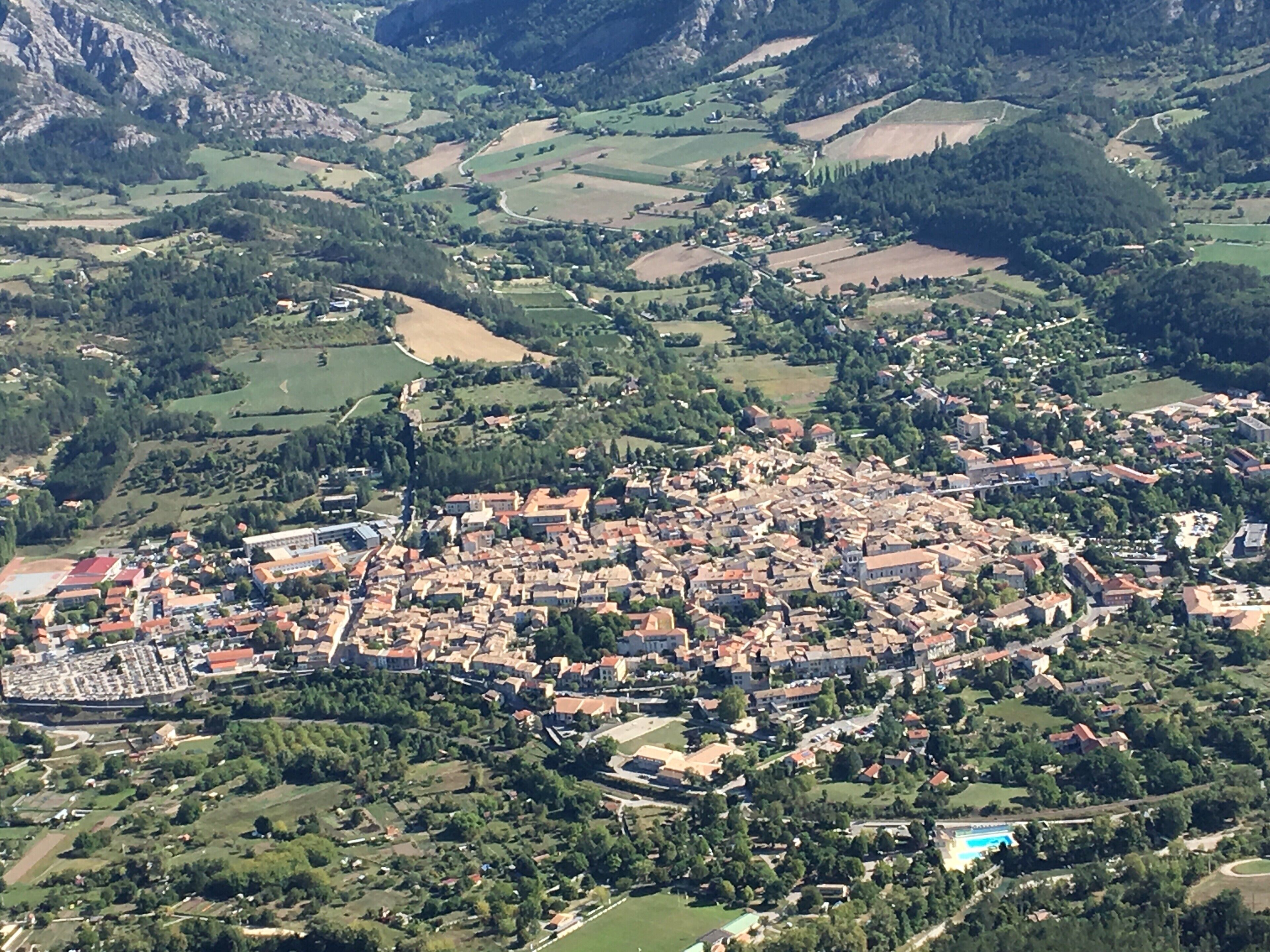 Eine Vogelperspektive zeigt eine Stadt mit einer dichten Bebauung, umgeben von grünen Feldern und Bergen.