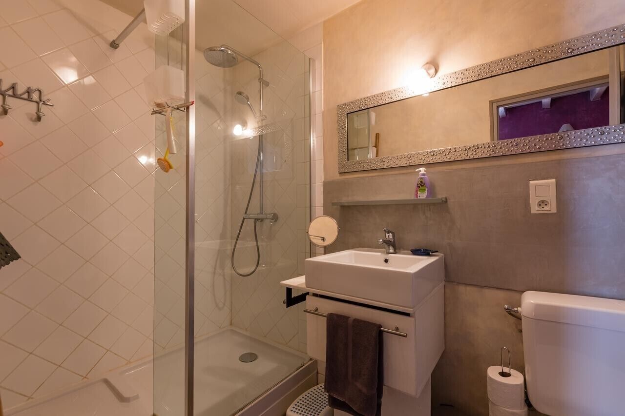 Une salle de bain avec une douche à parois de verre, un lavabo blanc, un miroir avec un cadre décoratif et des toilettes.