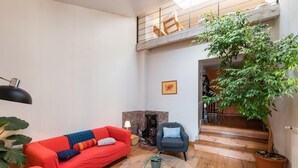 Un salon avec un canapé rouge, une table basse ronde, un fauteuil bleu, une cheminée et un escalier menant à un niveau supérieur.