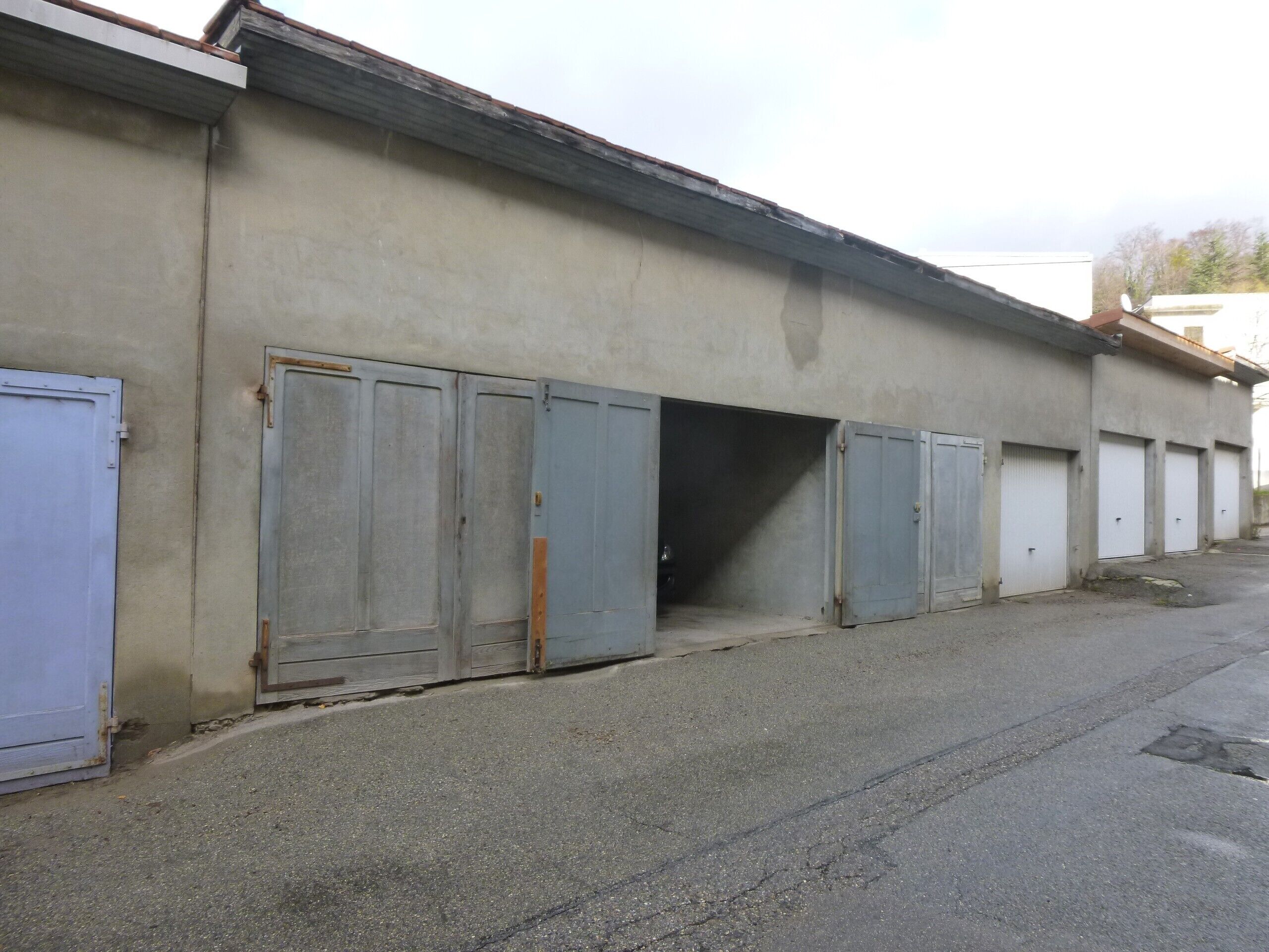 Une rangée de portes métalliques fermées, la façade d’un bâtiment en béton et un sol pavé.