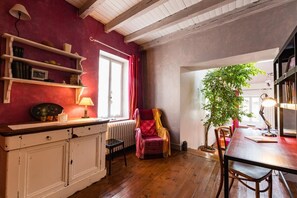 Una stanza accogliente con pavimento in legno, parete rossa, finestra con tende, una sedia, un tavolo e una libreria.