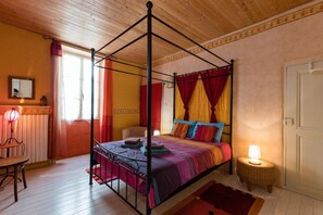 Un letto a baldacchino con tenda, un tavolino rotondo con una lampada, una sedia e un pavimento in legno.