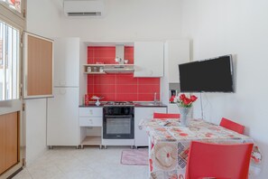 Une cuisine compacte avec des meubles blancs, un plan de travail rouge, une cuisinière et un coin repas comprenant une table et des chaises.