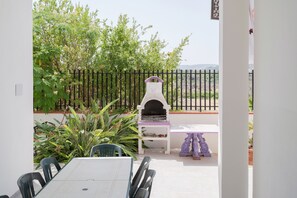 Une terrasse extérieure équipée d’un barbecue, d’une table à manger, de chaises et de plantes en pot.