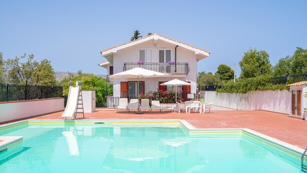 Ein zweistöckiges Haus mit Schwimmbecken, einer Rutsche und Gartenmöbeln.