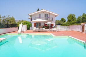 Une maison à deux étages avec une piscine, un toboggan et du mobilier d’extérieur.
