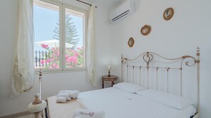 Ein Schlafzimmer mit einem Bett, einem Fenster, einem Nachttisch und einer Wand-Klimaanlage.