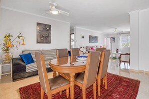 Un coin repas avec une table ronde, des chaises et un tapis rouge à motifs. On y trouve également un canapé avec un coussin bleu et un vase rempli de fleurs.