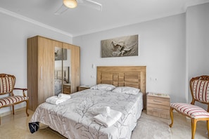 Une chambre à coucher avec un grand lit, une armoire, deux chaises, une table de chevet et une œuvre d’art accrochée au mur.