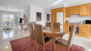 Una cocina moderna con armarios de madera, un comedor con una mesa y sillas redondas, y una sala de estar con sofá y televisor.